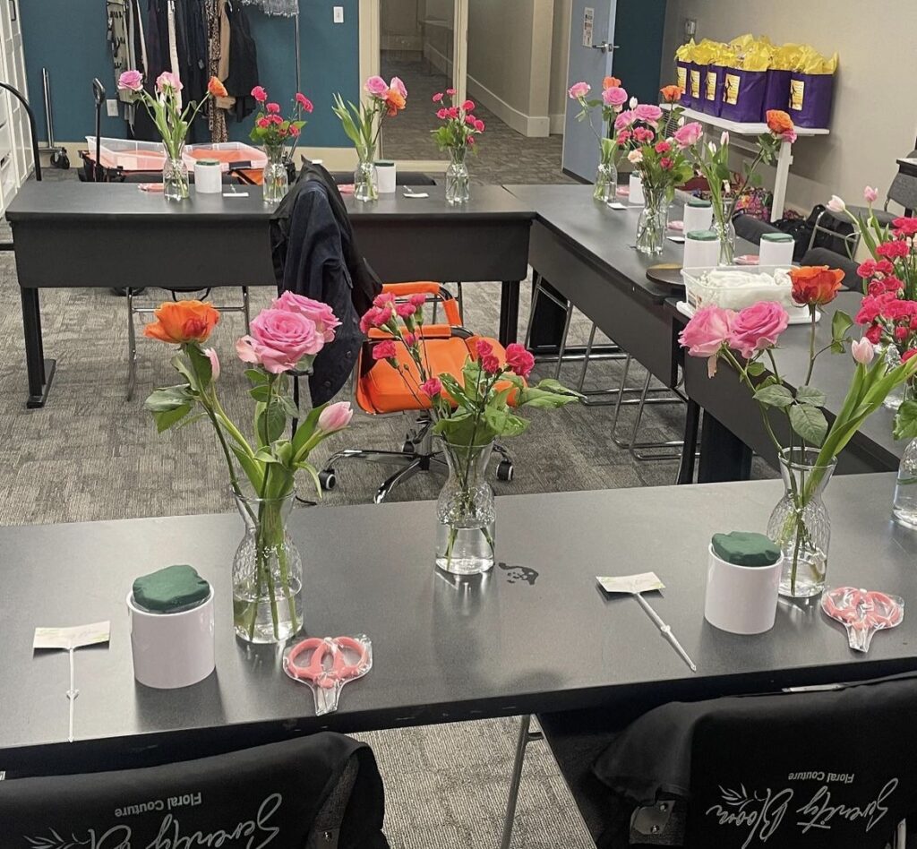 This photo of the workshop space shows black tables arranged together in a group, with vases of flowers assembled at each individual seating area