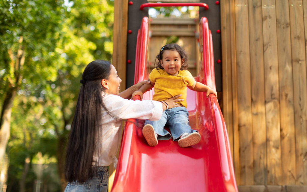 Mother-helping-young-child-down-a-red-slide